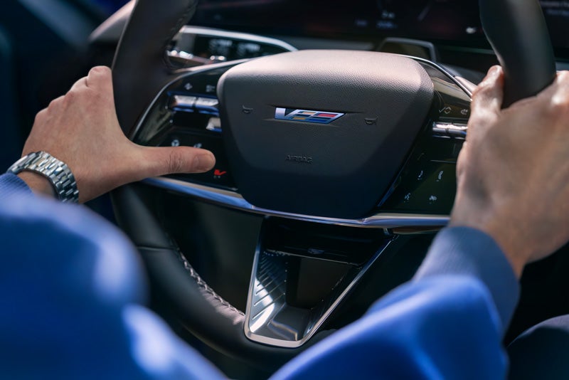 Close-up of a Man About to Press the V-Button on the 2026 OPTIQ-V Steering Wheel | Waldorf Cadillac in Waldorf MD